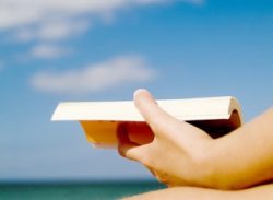 A woman's hand holding a book, on the beach