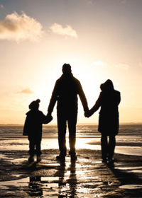 Silhouette of two adults and a child at the coast