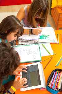 Three teenage girls busy with homework at desk.