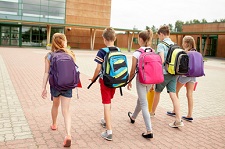 primary education, friendship, childhood and people concept - group of happy elementary school students with backpacks walking outdoors from back